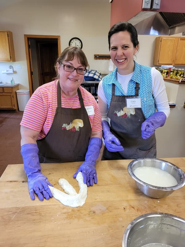 Two smiling students in aprons at a cheesemaking class